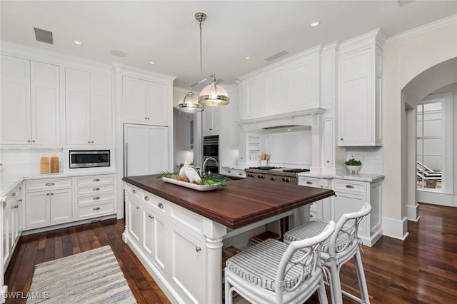 kitchen with appliances with stainless steel finishes, white cabinetry, decorative light fixtures, butcher block countertops, and a kitchen island with sink