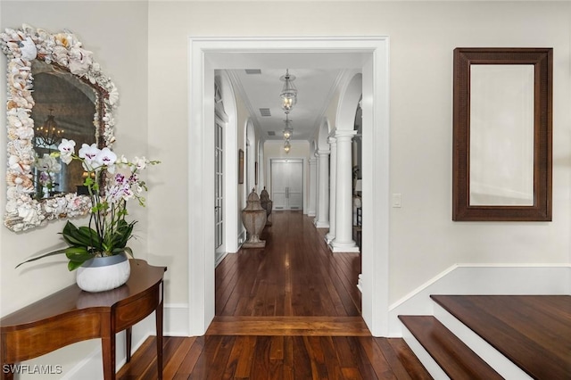 corridor featuring dark hardwood / wood-style floors, ornate columns, and ornamental molding