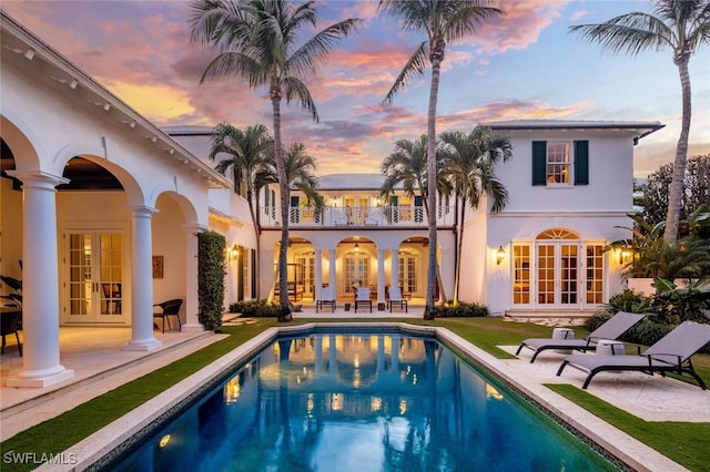 back house at dusk featuring a patio area, a balcony, and french doors