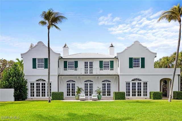 back of property featuring a balcony, french doors, and a lawn