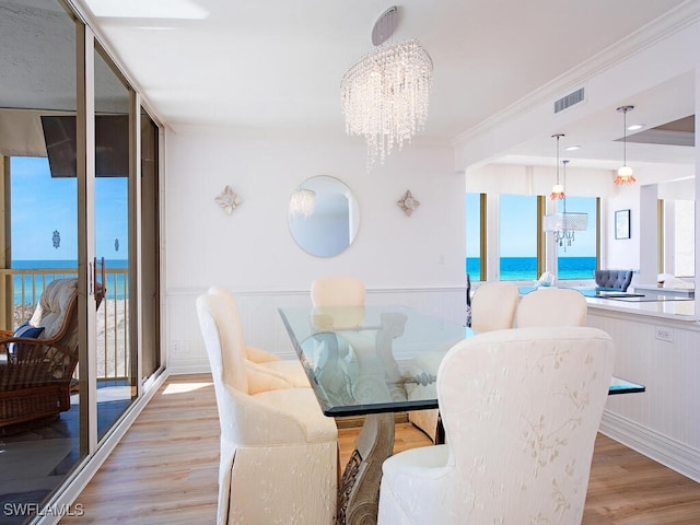 dining area featuring light hardwood / wood-style floors, a water view, crown molding, and a chandelier