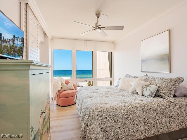 bedroom featuring ceiling fan, light hardwood / wood-style floors, a water view, and crown molding