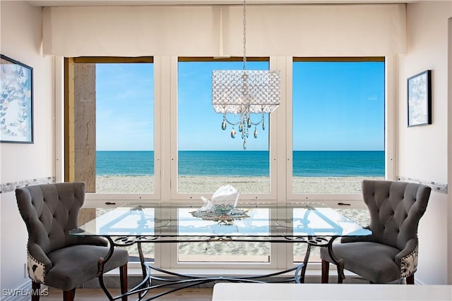 dining room featuring plenty of natural light, a water view, a view of the beach, and an inviting chandelier