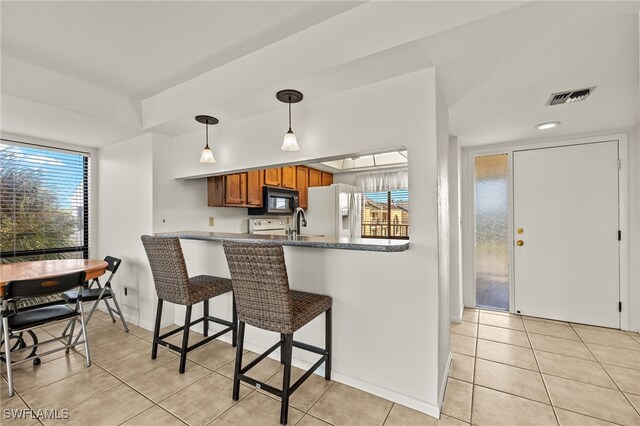 kitchen featuring a kitchen breakfast bar, hanging light fixtures, white fridge with ice dispenser, light tile patterned floors, and kitchen peninsula