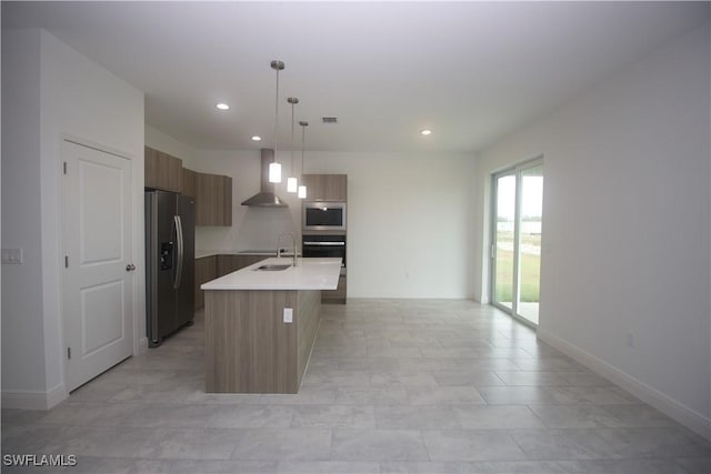 kitchen featuring a center island with sink, wall chimney range hood, sink, appliances with stainless steel finishes, and decorative light fixtures