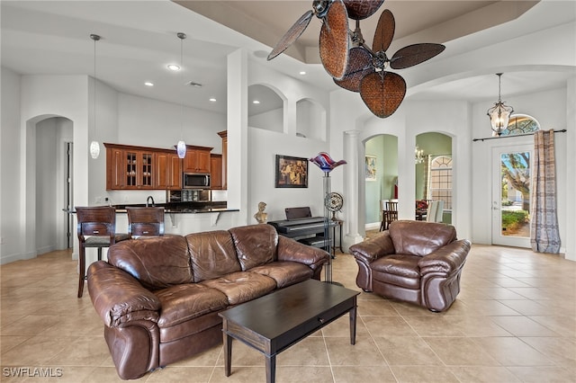 living room featuring ceiling fan with notable chandelier, light tile patterned floors, a high ceiling, and ornate columns