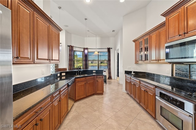 kitchen featuring sink, stainless steel appliances, dark stone counters, pendant lighting, and light tile patterned floors