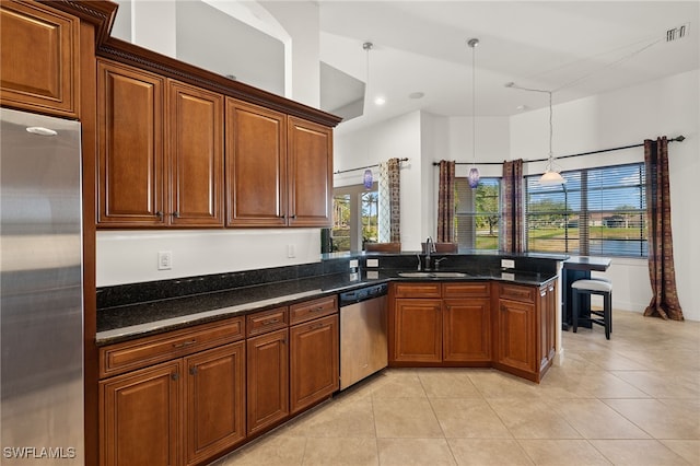 kitchen featuring sink, dark stone countertops, decorative light fixtures, light tile patterned flooring, and appliances with stainless steel finishes