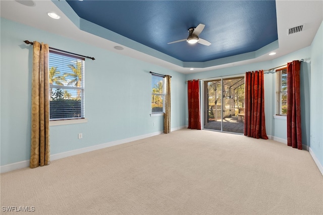 carpeted empty room with plenty of natural light, ceiling fan, and a tray ceiling