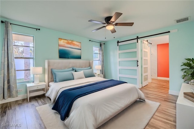 bedroom featuring a barn door, ceiling fan, light hardwood / wood-style flooring, and multiple windows