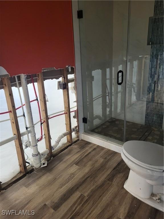 bathroom featuring hardwood / wood-style flooring, toilet, and a shower with shower door