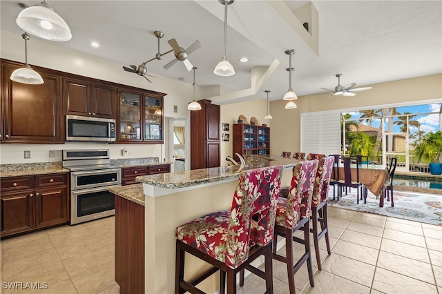 kitchen with pendant lighting, ceiling fan, light stone countertops, and stainless steel appliances