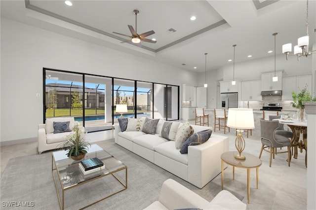 living room with a tray ceiling, a towering ceiling, and ceiling fan with notable chandelier