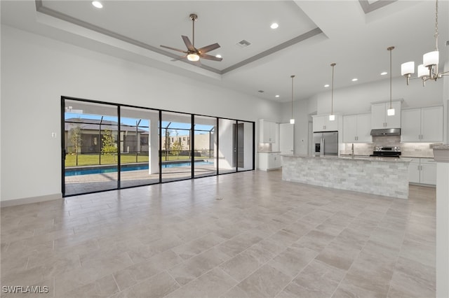 unfurnished living room featuring a high ceiling, a tray ceiling, and ceiling fan