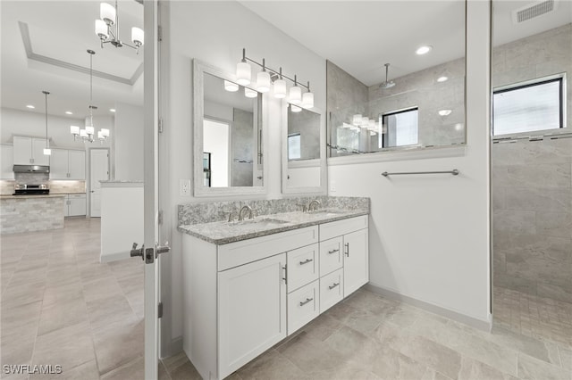 bathroom with a tray ceiling, an inviting chandelier, vanity, and tiled shower