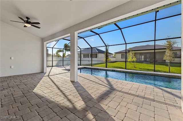 view of pool with glass enclosure, ceiling fan, a yard, and a patio