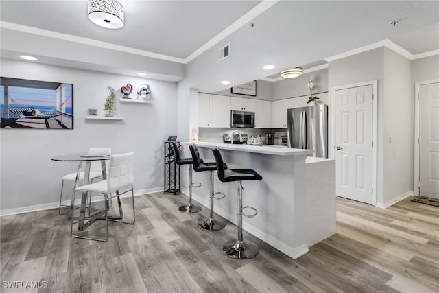 kitchen with kitchen peninsula, light hardwood / wood-style floors, a breakfast bar area, white cabinets, and appliances with stainless steel finishes