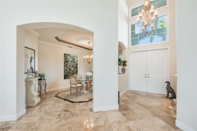 entryway featuring a raised ceiling, ornamental molding, a high ceiling, and a notable chandelier