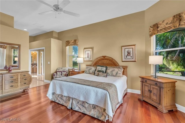 bedroom featuring multiple windows, ensuite bathroom, ceiling fan, and wood-type flooring