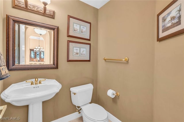 bathroom with toilet, sink, and an inviting chandelier