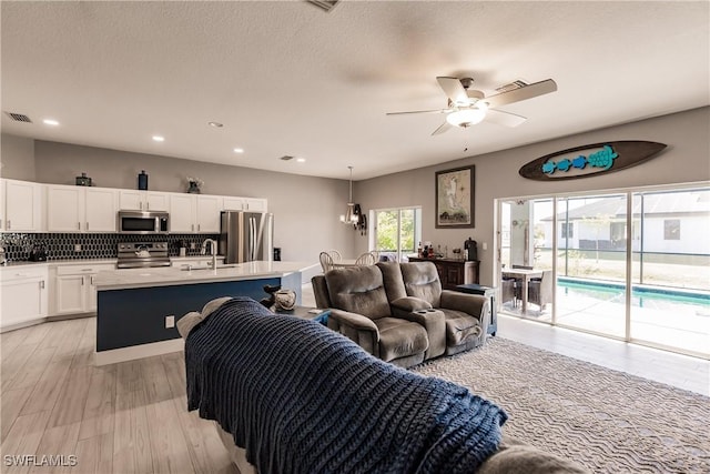 living room featuring ceiling fan, light hardwood / wood-style flooring, a textured ceiling, and sink