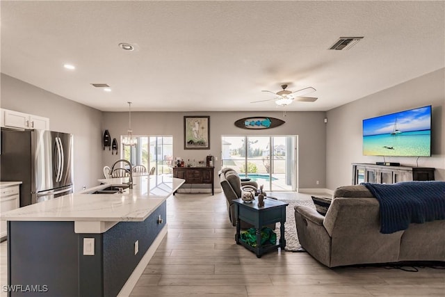 living room featuring a textured ceiling, ceiling fan with notable chandelier, wood-type flooring, and sink