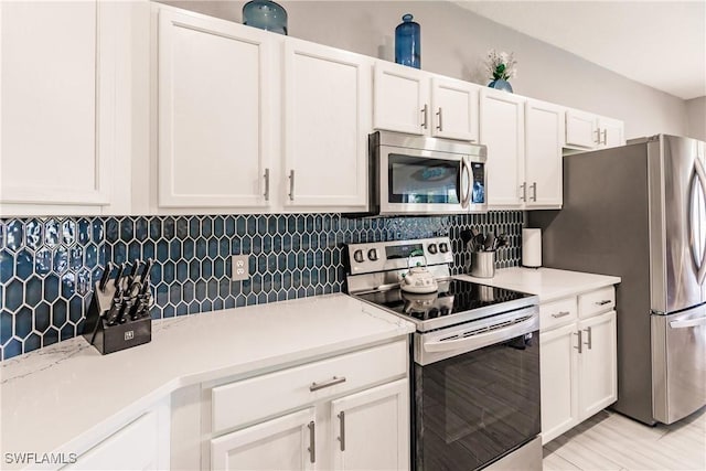 kitchen with white cabinets, appliances with stainless steel finishes, backsplash, and light hardwood / wood-style flooring