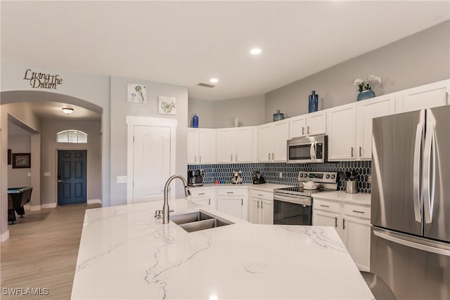 kitchen featuring light stone countertops, light wood-type flooring, stainless steel appliances, sink, and white cabinetry