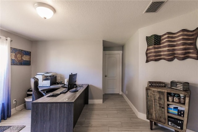 home office with light hardwood / wood-style floors and a textured ceiling