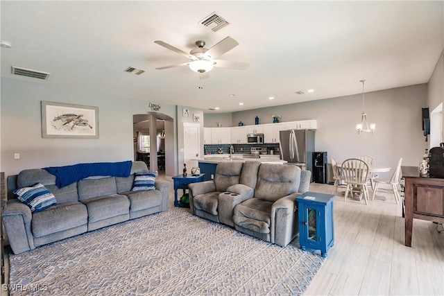 living room featuring sink, ceiling fan with notable chandelier, and light wood-type flooring