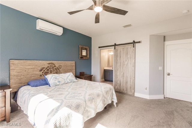 bedroom with a wall mounted air conditioner, light carpet, ensuite bath, ceiling fan, and a barn door