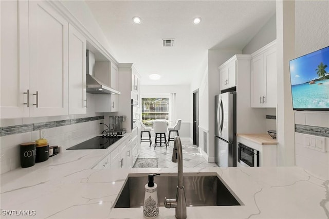 kitchen featuring light stone countertops, wall chimney exhaust hood, sink, black appliances, and white cabinets