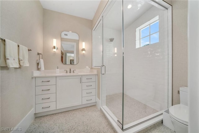 bathroom with toilet, a stall shower, vanity, baseboards, and speckled floor