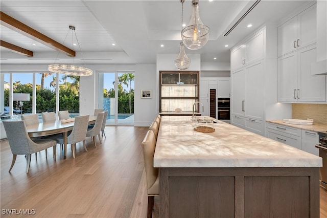 kitchen featuring a healthy amount of sunlight, a center island with sink, backsplash, and light wood-type flooring