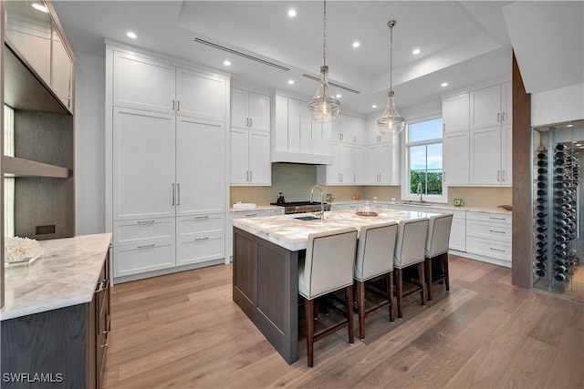 kitchen with an island with sink, a tray ceiling, white cabinets, and a breakfast bar area