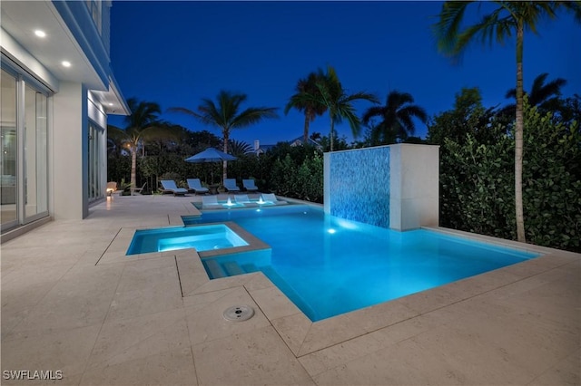 pool at twilight featuring a pool with connected hot tub and a patio area