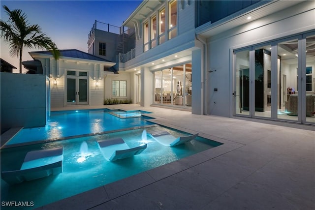 pool at dusk featuring a patio, french doors, and a pool with connected hot tub