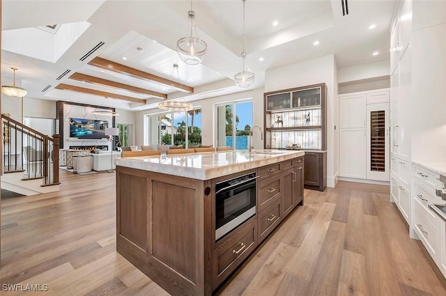 kitchen with light wood finished floors, hanging light fixtures, open floor plan, and a kitchen island with sink