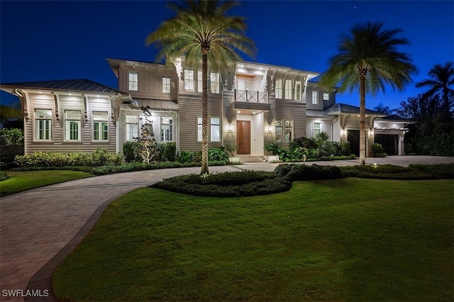 view of front of property featuring a standing seam roof, a balcony, a yard, and decorative driveway