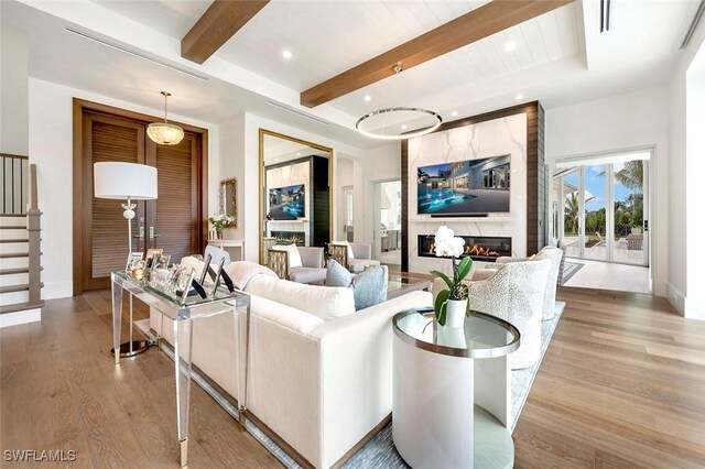 living room with a high end fireplace, wood finished floors, beamed ceiling, stairs, and recessed lighting