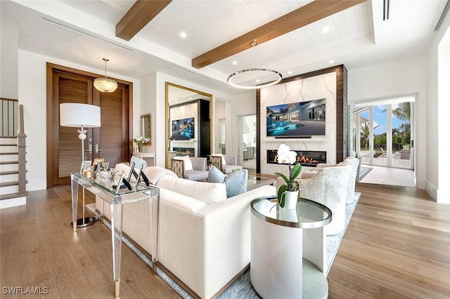 living area featuring stairway, wood finished floors, a premium fireplace, beam ceiling, and recessed lighting