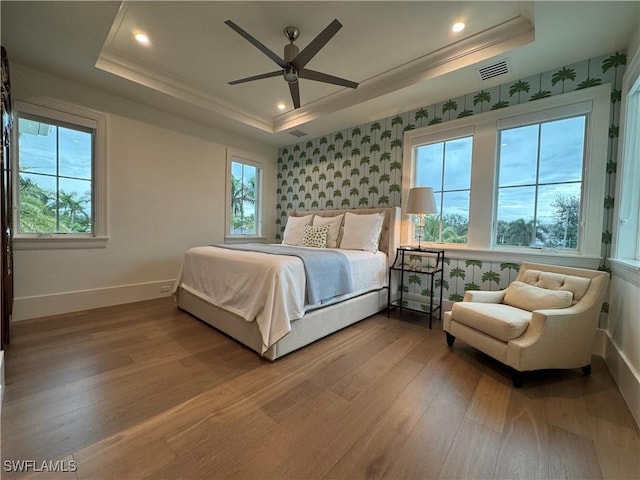 bedroom featuring a tray ceiling, wood finished floors, visible vents, and wallpapered walls