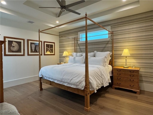 bedroom featuring wallpapered walls, baseboards, visible vents, a raised ceiling, and wood finished floors