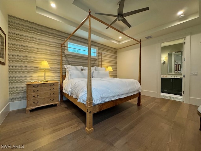 bedroom with a raised ceiling, wood finished floors, visible vents, and baseboards