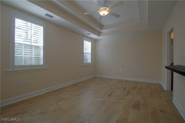 empty room featuring a tray ceiling, ceiling fan, and light hardwood / wood-style floors