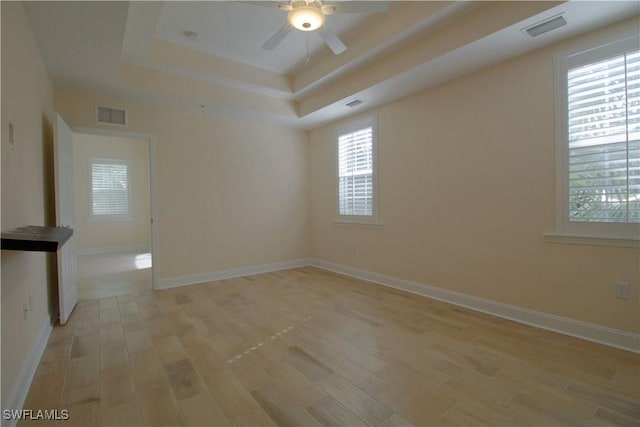 unfurnished room with a tray ceiling, a healthy amount of sunlight, and light hardwood / wood-style floors