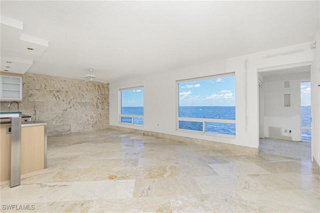 unfurnished living room featuring a water view, tile walls, and ceiling fan