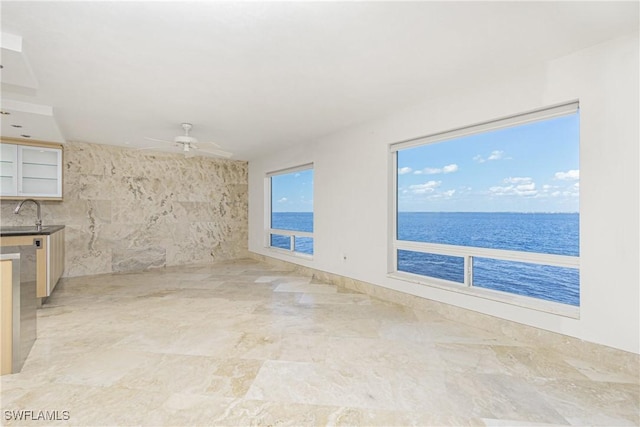 empty room with sink, a water view, tile walls, and ceiling fan