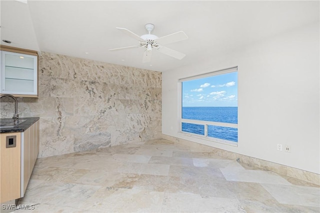 spare room featuring ceiling fan, a water view, sink, and tile walls