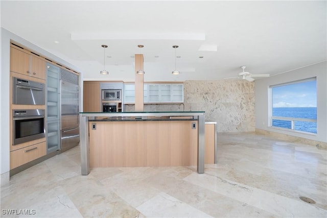 kitchen with light brown cabinetry, ceiling fan, built in appliances, a water view, and hanging light fixtures